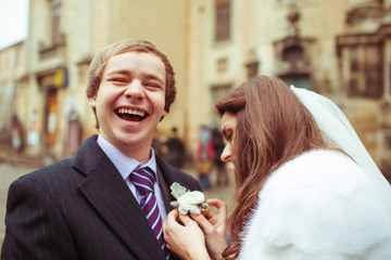 Funny young groom smiles broad while bride puts a pastel boutonn