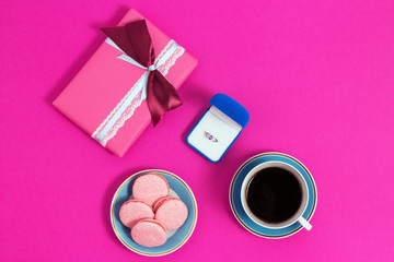 Obraz na płótnie Canvas Coffee with macarons and ring on a pink background. An offer of marriage. Top view, toned image
