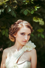 Goddess bride poses in diadem among green tree branches