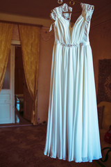 White wedding dress hangs on the peg in big room