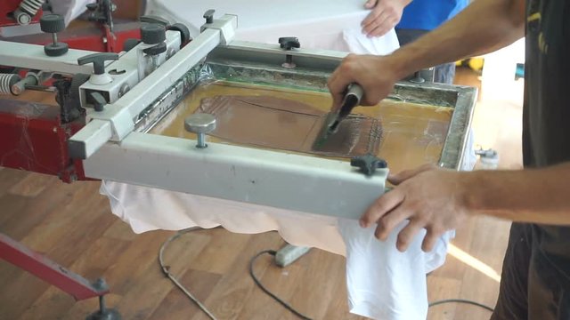 Screen printing manufacturing on t-shirts. Worker print an image on fabric on a hand bench. Image creating process