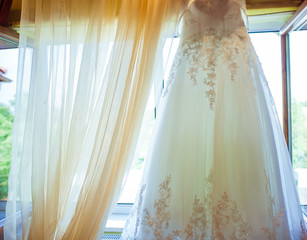 White curtain hides gorgeous wedding dress hanging on the window