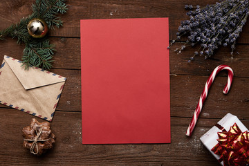 Christmas letter delivery concept. Red empty paper with gift box, candy, fir, cookies on wooden background. 