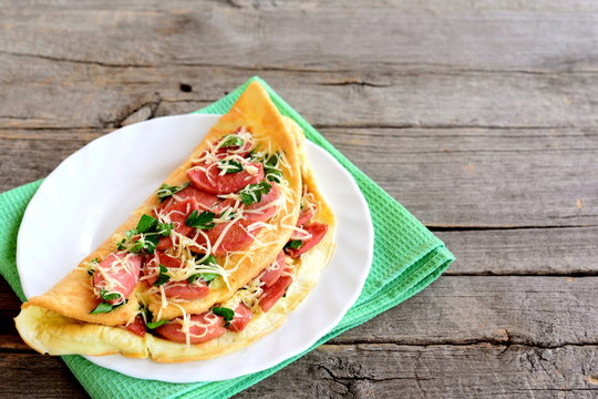 Hearty stuffed omelet on a plate. Omelet stuffed with sausage, cheese and parsley on an old wooden background with empty space for text. Nutritious breakfast recipe