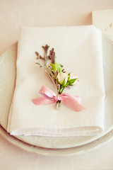 Fototapeta na wymiar Tiny rose buds with pink ribbon lie on the white dinner plate