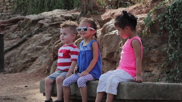 Siblings sitting on a bench posing for pictures, making funny faces, Park Guell in Barcelona, Spain.