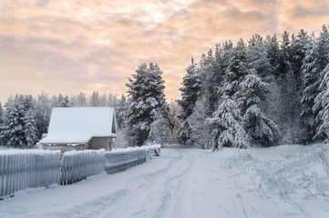 Village is in northern woods of Karelia, winter road with wooden house at evening. Russia