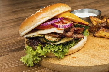 Homemade hamburger with fresh vegetables, potato and sauce on wooden table. 