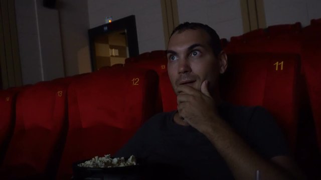 Thrilled man watching movie at cinema eating pop corn