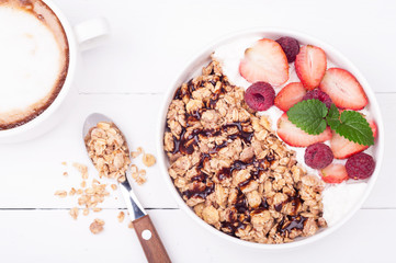 Oatmeal granola for breakfast with berries, yogurt and chocolate on white wooden background. Healthy eating. Top view