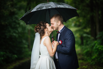 Bride and groom holding umbrella in hands looking at each other kissing and smiling