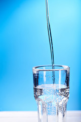 Pouring water with spashes in glass at a blue background