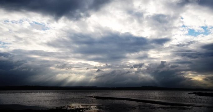 Sunbeams through moody clouds over water time-lapse