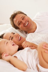 Smiling young family lying on bed at home