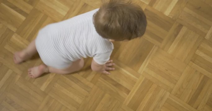 Vertical tracking shot of a cute baby crawling on the wooden floor.
