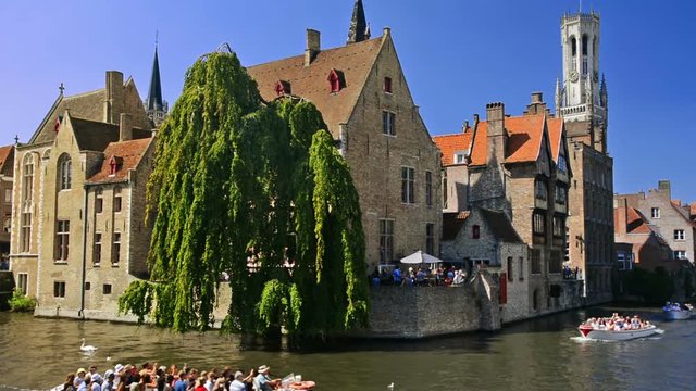 Cityscape of the canals of Bruges on a sunny day with Belfry in the background.