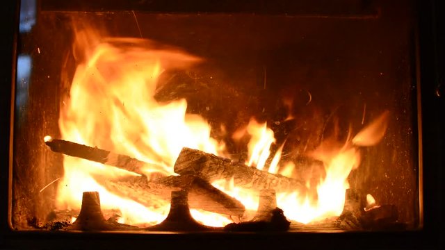 Closeup of burning logs in fireplace on dark black background.