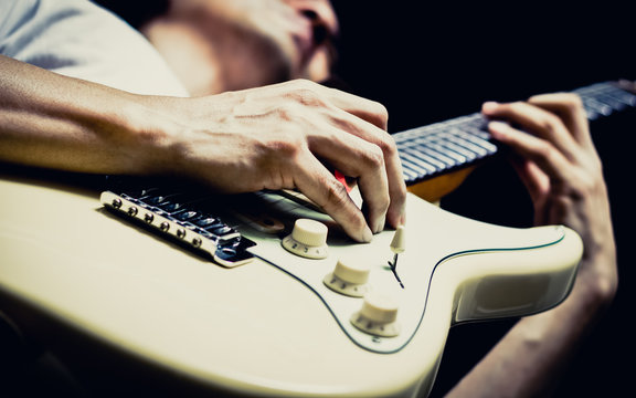 asian male musician playing white electric guitar on stage