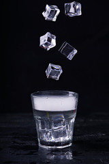 Hot water with a lot of steam in a glass and ice cubes in motion at a black background. Dark photo. Concept photo: three state of water - ice, water, steam.