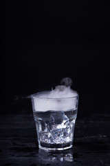 Hot water with a lot of steam in a glass at a black background. Dark photo. Concept photo: three state of water - ice, water, steam.