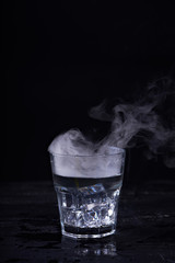 Hot water with a lot of steam in a glass at a black background. Dark photo. Concept photo: three state of water - ice, water, steam.
