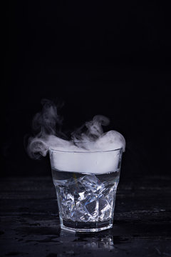 Hot Water With A Lot Of Steam In A Glass At A Black Background. Dark Photo. Concept Photo: Three State Of Water - Ice, Water, Steam.