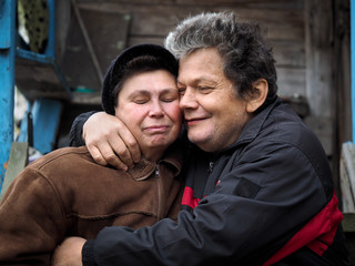 The man affectionately hugs a woman. People aged. Old wooden house