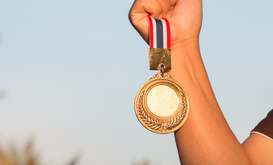 hand raised and holding gold medal against sky. award concept