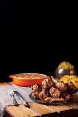 Close view of grilled chicken legs, knife, and fork mash potatoes, pumpkin pie on a table on a black background. Dark photo. Vertical shot