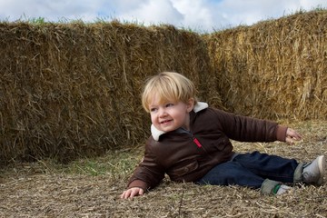 Naklejka na ściany i meble adorable young toddler boy sitting by haystacks on farm in fall autumn season