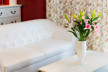 flowers in white vase on table,white leather sofa armchair & flowers pattern curtain, cozy living room