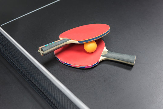 table tennis racket with orange ball on black