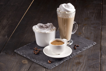 Espresso, cappuccino and latte cups are together on the wooden table.