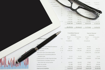 ball pen, glasses and Smart teblet on financial documents.