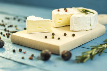 Round camembert cheese mold with rosemary on wooden board