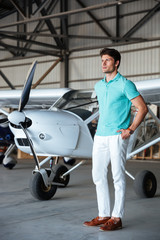 Serious attractive young man standing in front of small aircraft