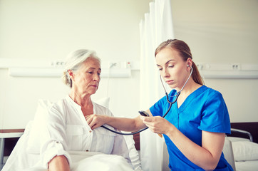 nurse with stethoscope and senior woman at clinic