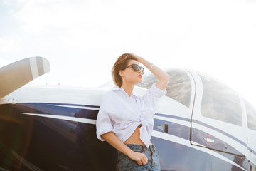 Woman in sunglasses standing outdoors near small private plane