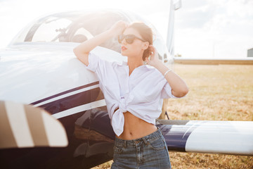 Obraz premium Woman in sunglasses standing outdoors near small plane