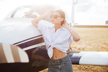 Woman in sunglasses standing outdoors near small plane