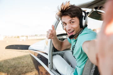 Tuinposter Cheerful pilot sitting in airplane cabin and showing thumbs up © Drobot Dean