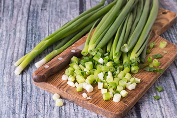  Green onion.   Green onion and a knife on a cutting board on an old wooden table.