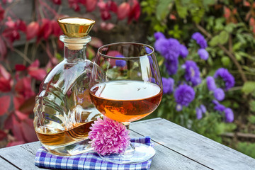 Bottle and snifter brandy with flower on table in garden
