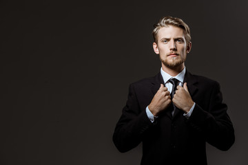 Young successful businessman correcting jacket over grey background. 