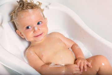 Little pretty wet baby boy in bath room sitting and smiling on white background.