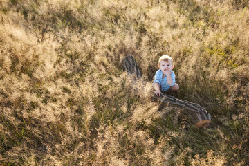 One year old baby boy in a meadow climbing a log at sunset.