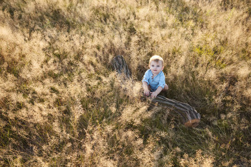 Naklejka na ściany i meble One year old baby boy in a meadow climbing a log at sunset.