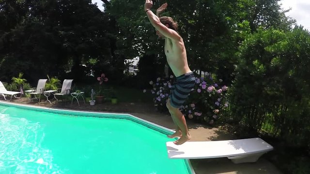 Young man does front flip dive into backyard pool, summer pool party in slow motion.