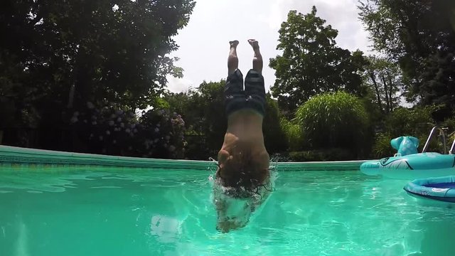 Young man dives off diving board, backyard summer pool party in slow motion.