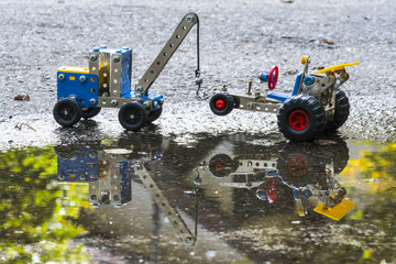 Toy tow truck lifts car, both built with small pieces of metal and plastic. Roadside assistance concept.